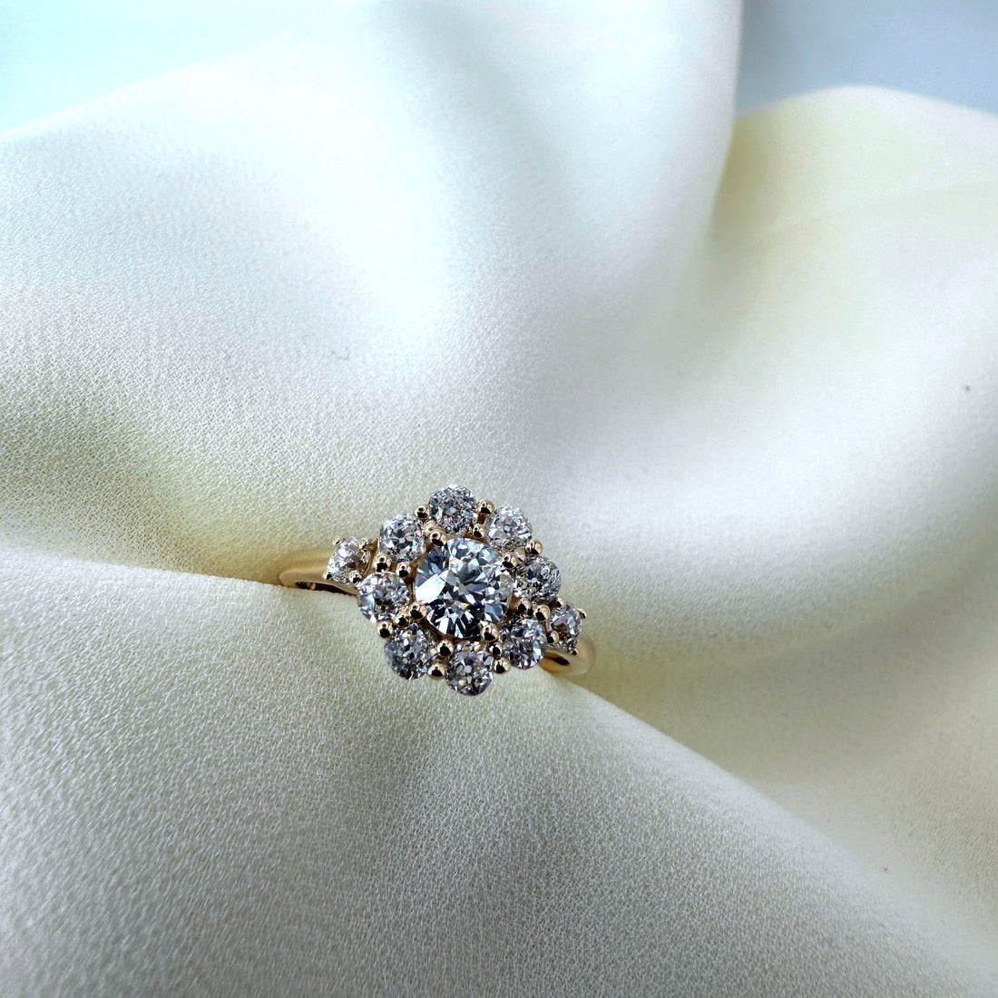 A bespoke gold engagement ring, made from a family heirloom. In the centre is a large diamond. The diamond is surrounded by smaller diamonds creating an oval shape.