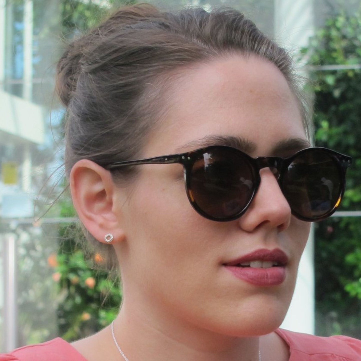 Woman wearing delicate silver circle earring studs, sunglasses and pink lipstick