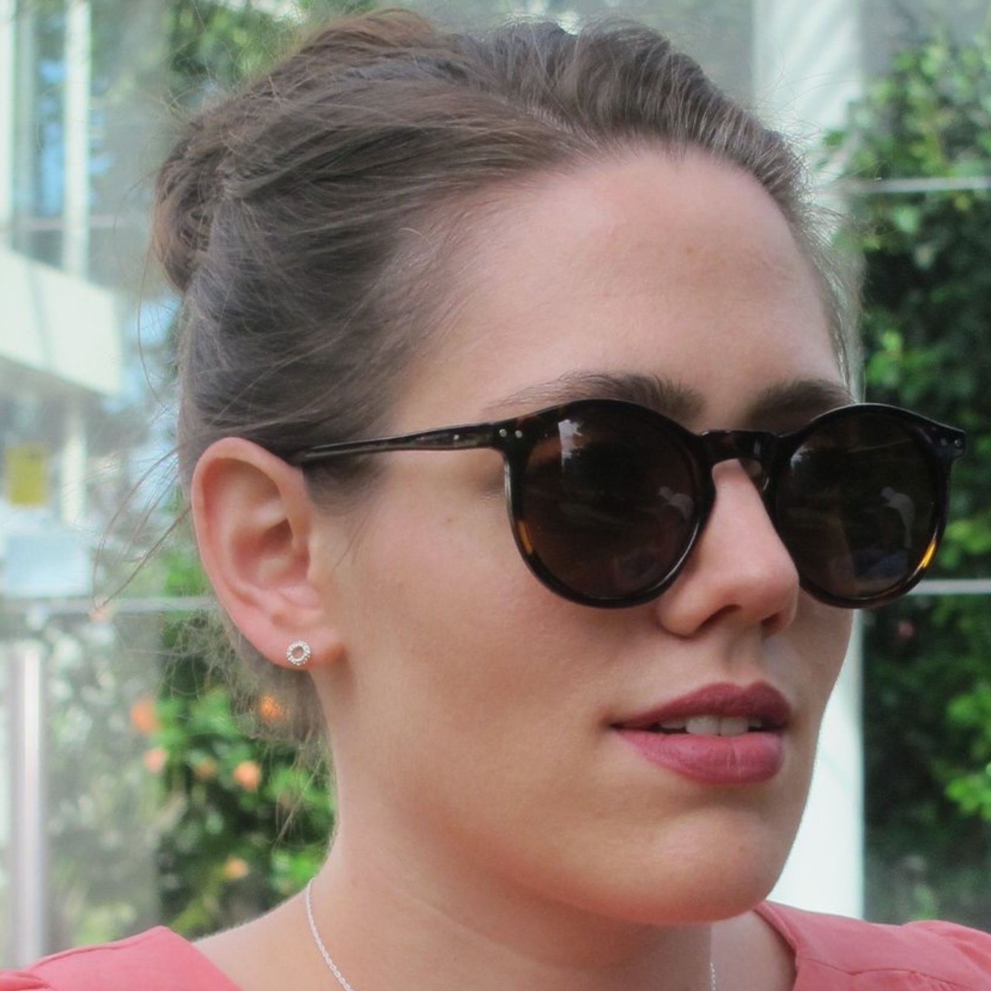 Woman wearing delicate silver circle earring studs, sunglasses and pink lipstick