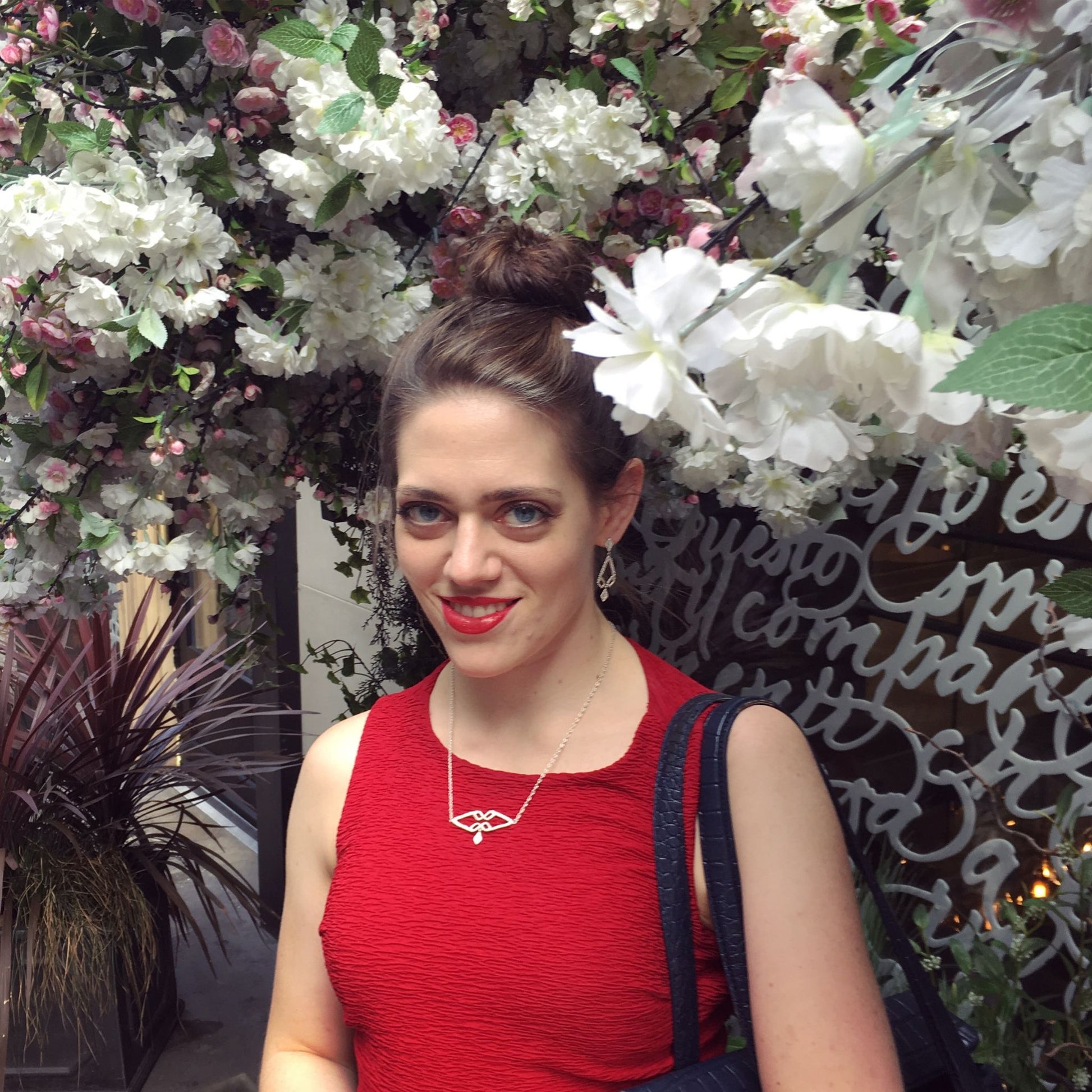 woman wearing a red dress and geometric silver earrings and necklace in front of an instagramable flower display