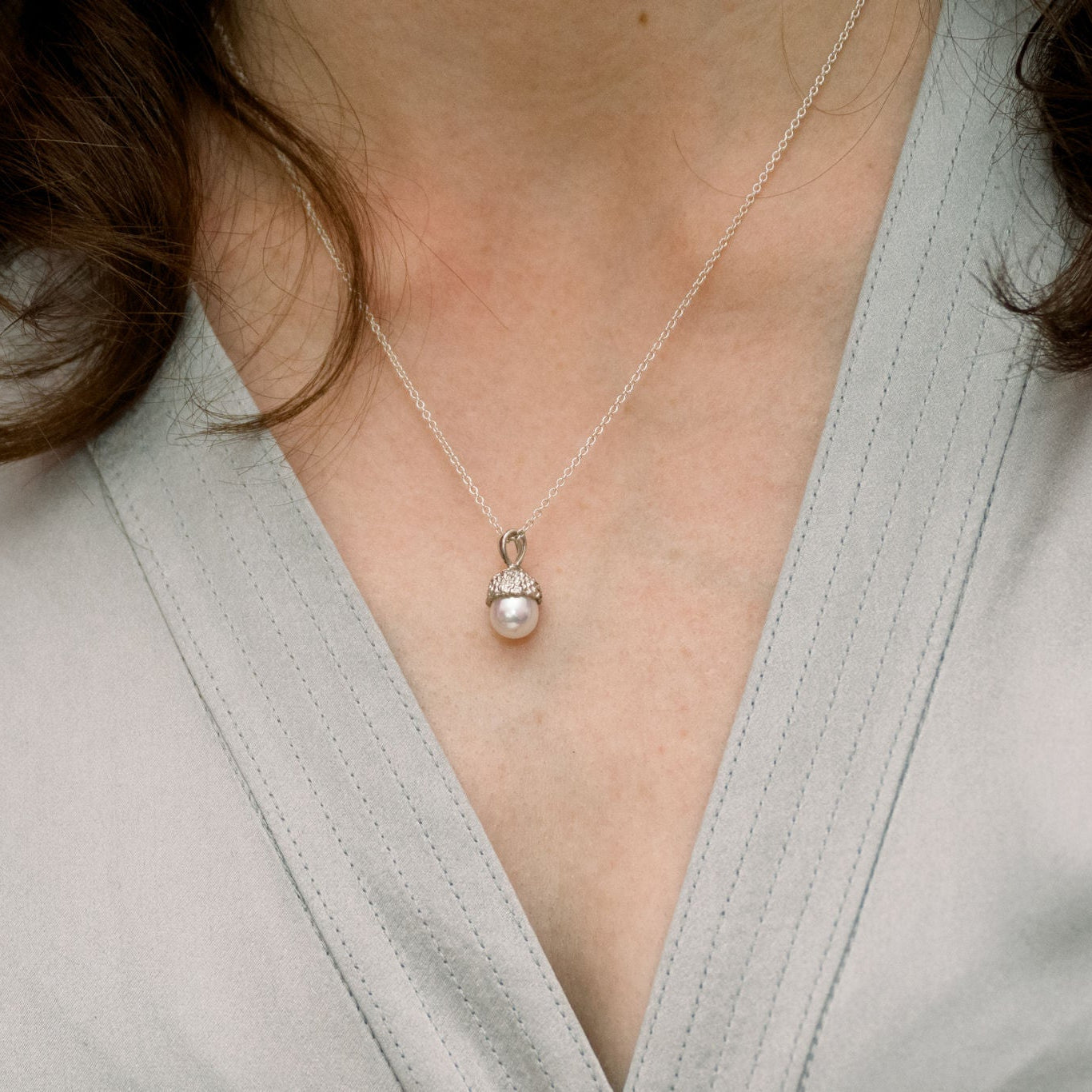 Pearl acorn necklace, set in hand-stitched sterling silver, worn by a person in a light gray outfit