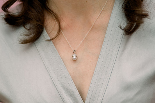 Pearl acorn necklace, set in hand-stitched sterling silver, worn by a person in a light gray outfit