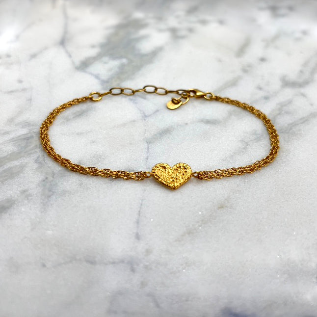 On a large piece of marble, there is a gold bracelet with a textured gold heart as the motif. The heart was originally stitched in lace and then cast in gold. The bracelet chain is multi-stranded.