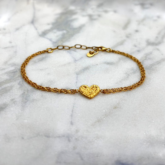 On a large piece of marble, there is a gold bracelet with a textured gold heart as the motif. The heart was originally stitched in lace and then cast in gold. The bracelet chain is multi-stranded.