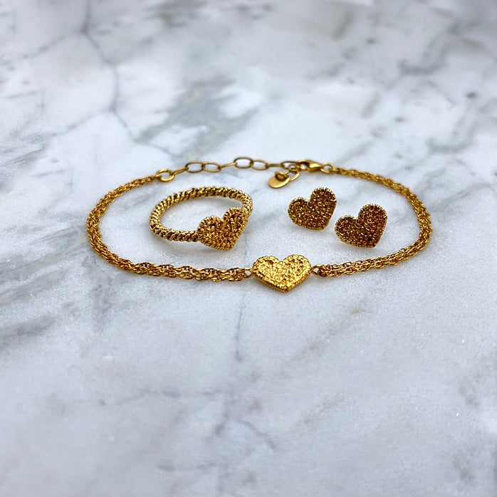 On a large piece of marble, there is a gold bracelet, ring and stud earring set. The motif for each is a textured gold heart, originally stitched in lace and then cast in gold. The ring has a twisted gold band made to look like rope.