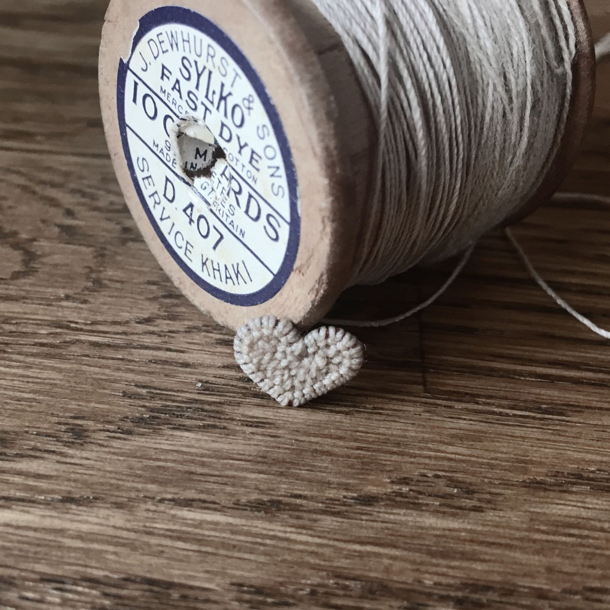 micro crochet heart in front of a vintage cotton spool cast into gold and silver